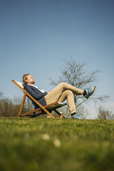Oberflächenansicht eines männlichen Berufstätigen, der sich an einem sonnigen Tag im Park auf einem Stuhl ausruht - JOSEF01458