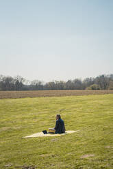Businessman sitting on picnic blanket at park during sunny day - JOSEF01463