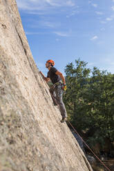Von unten Mann klettert mit Kletterausrüstung auf einen Felsen in der Natur - ADSF10182