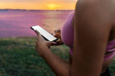 Close-up of fit woman using smart phone during sunset - MGOF04368
