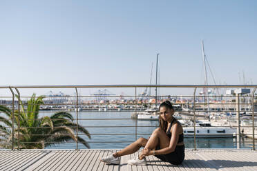 Woman sitting on boardwalk in sports clothing during sunny day - EGAF00639