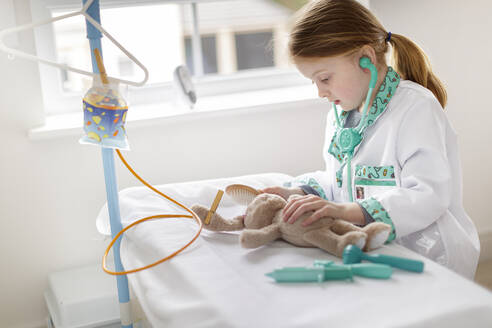 Junges Mädchen als Ärztin verkleidet, die vorgibt, ein Kuscheltier in einem fiktiven Krankenhausbett zu behandeln - MINF15025