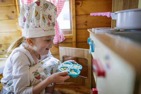 Junges Mädchen in wendy Haus setzen Tasse Kuchen in den Ofen vorgibt, in der Küche zu kochen - MINF15026