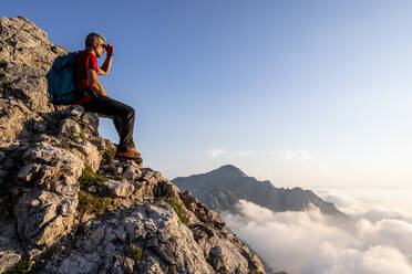 Wanderer betrachtet die Aussicht, während er auf einem Berg in den Bergamasker Alpen, Italien, sitzt - MCVF00554