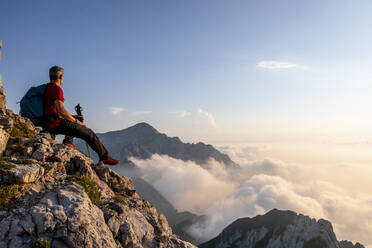 Wanderer bewundert die Aussicht, während er auf dem Gipfel eines Berges in den Bergamasker Alpen, Italien, sitzt - MCVF00556