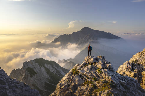 Wanderer, der auf einem Berggipfel in den Bergamasker Alpen, Italien, steht und die atemberaubende Aussicht bewundert - MCVF00557