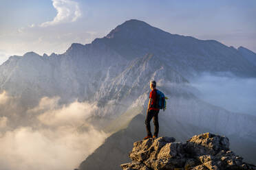 Mann steht auf dem Gipfel eines Berges in den Bergamasker Alpen, Italien - MCVF00558