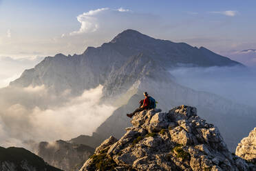Hiker sitting on mountain peak at Bergamasque Alps, Italy - MCVF00560