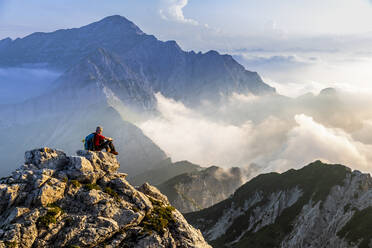 Mann sitzt und bewundert die Berglandschaft bei Sonnenaufgang in den Bergamasker Alpen, Italien - MCVF00562