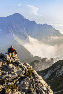 Wanderer bewundert die Aussicht, während er auf einem Berggipfel in den Bergamasker Alpen, Italien, sitzt - MCVF00563