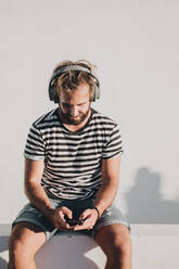 Junger Mann sitzend mit Smartphone und Kopfhörern - ADSF10227