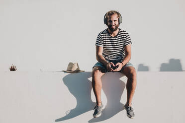 Young male sitting with smartphone and headphones - ADSF10228