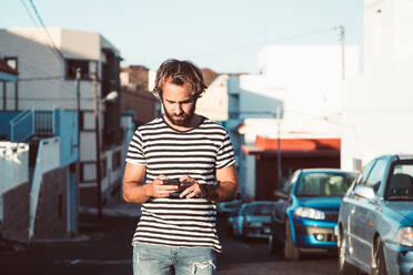 Handsome man in striped t-shirt browsing in smartphone while walking in La Restinga, El Hierro, on Canary Island - ADSF10232