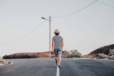 Rückenansicht eines trendigen Mannes in Shorts und T-Shirt auf einer verlassenen Straße in La Restinga, El Hierro - ADSF10240