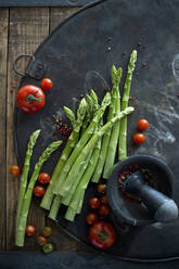 Mörser und Stößel, Pfefferkörner, Tomaten und Spargelstangen auf rustikalem Backblech - ASF06658