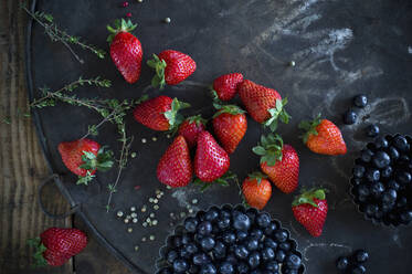 Thyme, peppercorn, blueberries and strawberries on rustic baking sheet - ASF06665