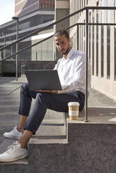 Geschäftsmann arbeitet an einem Laptop, während er auf einer Treppe sitzt - VEGF02630