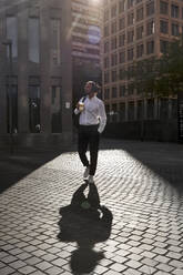 Geschäftsmann mit Kopfhörern trinkt Kaffee beim Spaziergang in der Stadt - VEGF02632