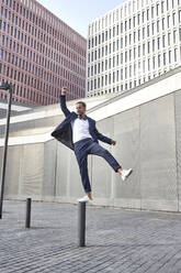 Happy businessman balancing on pole in city - VEGF02636