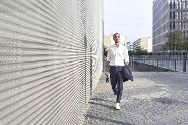 Businessman with headphones walking in city - VEGF02645