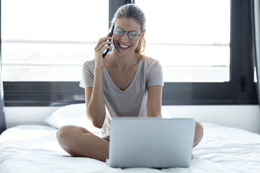 Blond woman using laptop and smartphone at home - JSRF00990