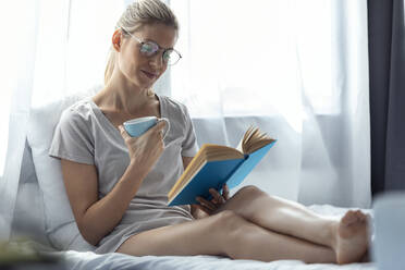 Blond woman reading a book in bed - JSRF00992
