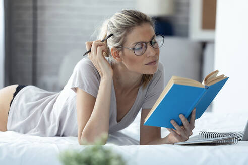 Blonde Frau liest ein Buch im Bett liegend - JSRF00995