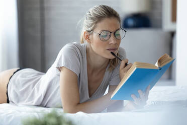 Blond woman reading a book lying in bed - JSRF00996