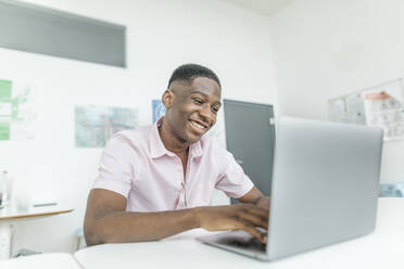 Lächelnder Geschäftsmann bei der Arbeit am Laptop am Arbeitsplatz - KMKF01456