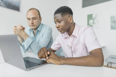 Coworkers working on laptop while sitting at workplace - KMKF01458