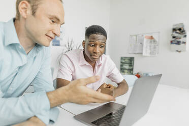 Colleagues working on laptop while sitting in office - KMKF01460