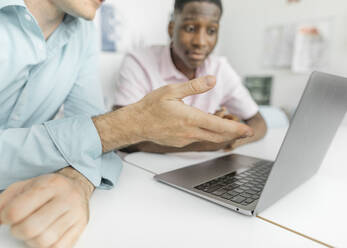 Colleagues working on laptop over table while sitting in office - KMKF01461