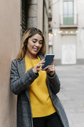 Junge Frau lehnt an der Wand und benutzt ihr Smartphone in der Stadt - RDGF00013