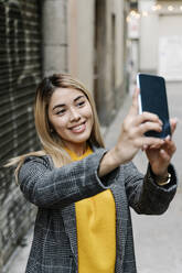 Junge Frau macht Selfie mit ihrem Smartphone in der Stadt - RDGF00014