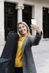Young woman with violin case taking selfie in city - RDGF00023