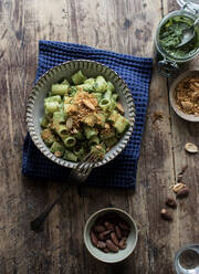 From above bowl of palatable pasta paccheri with fresh kale pesto and ground peanuts on timber tabletop - ADSF10335