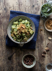 Von oben Schüssel mit schmackhaften Nudelpaccheri mit frischem Grünkohlpesto und gemahlenen Erdnüssen auf Holztischplatte - ADSF10335