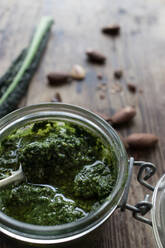 Nahaufnahme Glasgefäß mit leckerem Grünkohlpesto auf Holztischplatte neben frischen Erdnüssen - ADSF10339