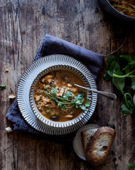 Pieces of bread and fresh parsley placed on wooden tabletop near bowl with yummy quinoa soup - ADSF10346