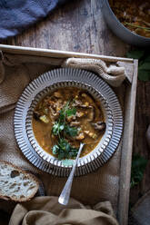 Pieces of bread and fresh parsley placed on wooden tabletop near bowl with yummy quinoa soup - ADSF10347