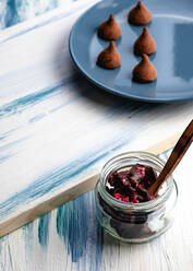 Von oben Glasgefäß mit köstlichen Schokoladenstückchen mit Marmelade und hausgemachten Schokoladentrüffeln auf Teller auf Holztisch - ADSF10397