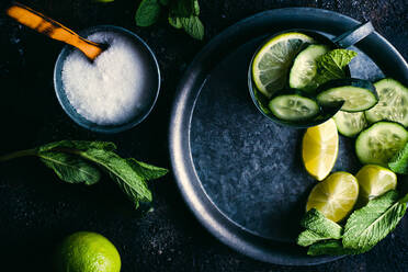 Top view of cup of sugar with spoon placed on dark table near tray with mug of fresh cucumber detox drink with mint and lime - ADSF10399