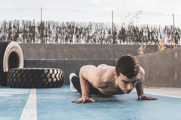 Muskulöser junger Mann, der Liegestütze macht, während er auf dem Betonboden eines Sportplatzes in der Stadt trainiert - ADSF10402