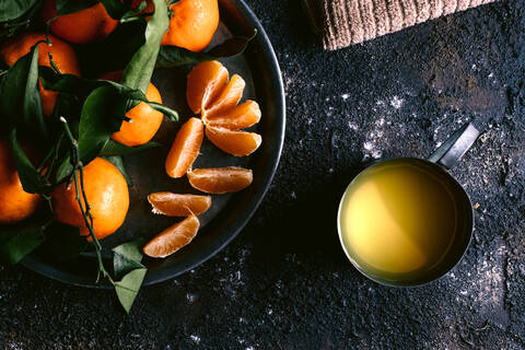 Top view of mug with fresh fruit juice and plate with ripe tangerines placed on rough black table near napkin stock photo