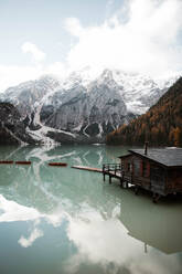 Holzhaus auf Stelzen und Boote auf nebligem See mit Spiegelung der mächtigen Dolomiten in Italien - ADSF10412