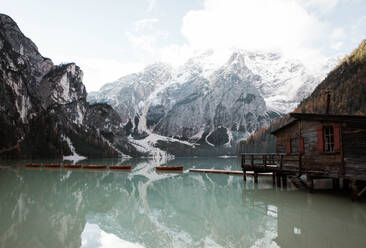 Holzhaus auf Stelzen und Boote auf nebligem See mit Spiegelung der mächtigen Dolomiten in Italien - ADSF10413