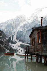 Holzhaus auf Stelzen und Boote auf nebligem See mit Spiegelung der mächtigen Dolomiten in Italien - ADSF10414