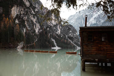 Holzhaus auf Stelzen und Boote auf nebligem See mit Spiegelung der mächtigen Dolomiten in Italien - ADSF10428