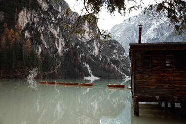 Wooden house on stilts and boats on nebulous lake with reflection of powerful Dolomites mountains at Italy - ADSF10428