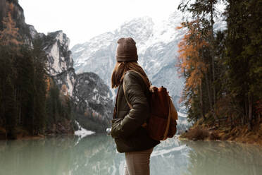 Rückenansicht einer anonymen Reisenden in Freizeitkleidung mit Rucksack, die sich am Anblick eines türkisfarbenen Sees mit nebligen Dolomitenbergen im Hintergrund in Italien erfreut - ADSF10429